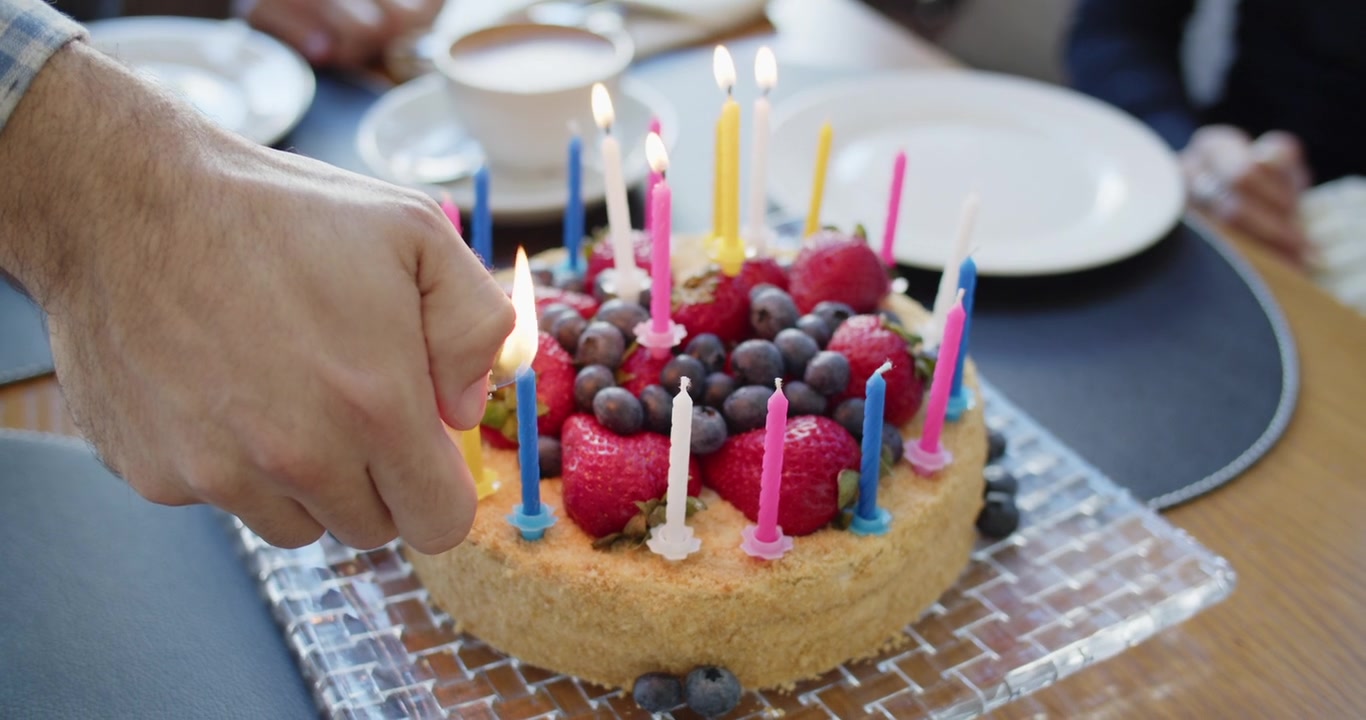 Manos encendiendo las velas de una tarta con frutos rojos, sin mostrar rostros