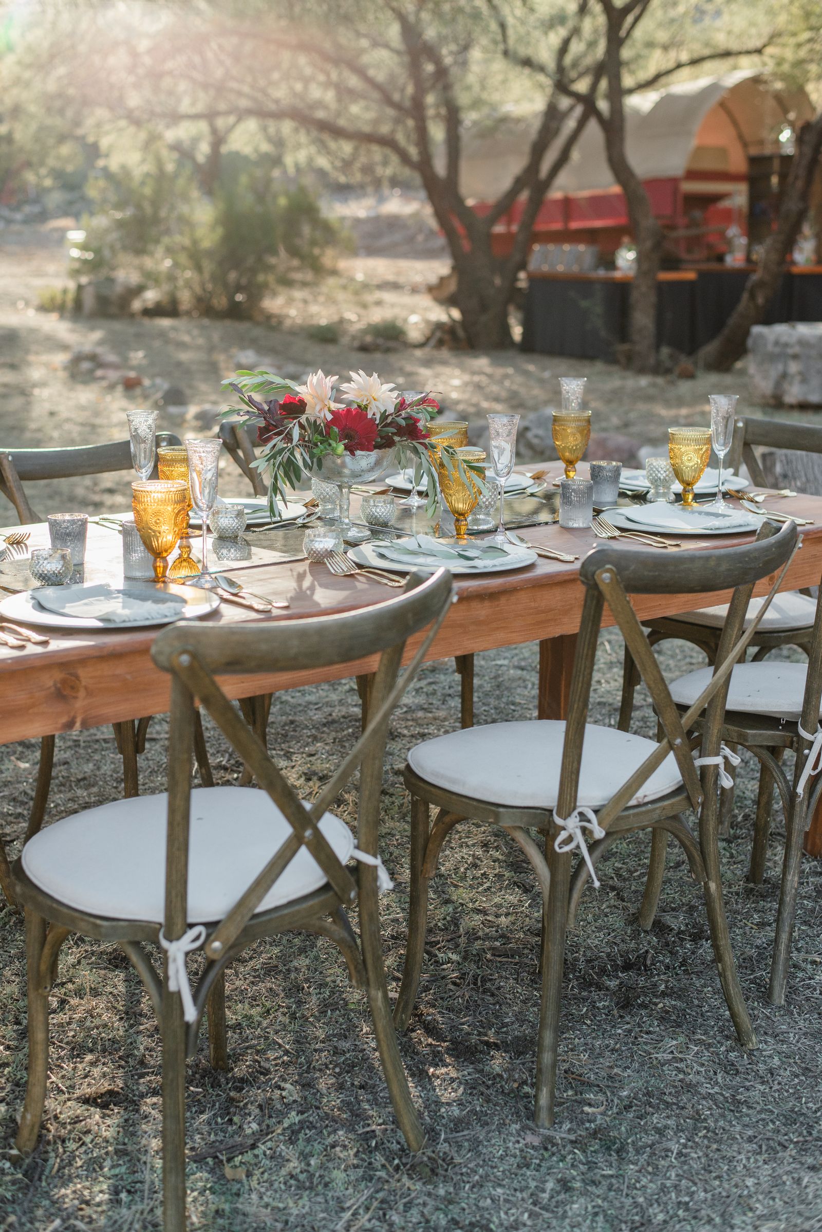 Mesa preparada en un jardín con flores y vajilla para una celebración íntima, sin personas